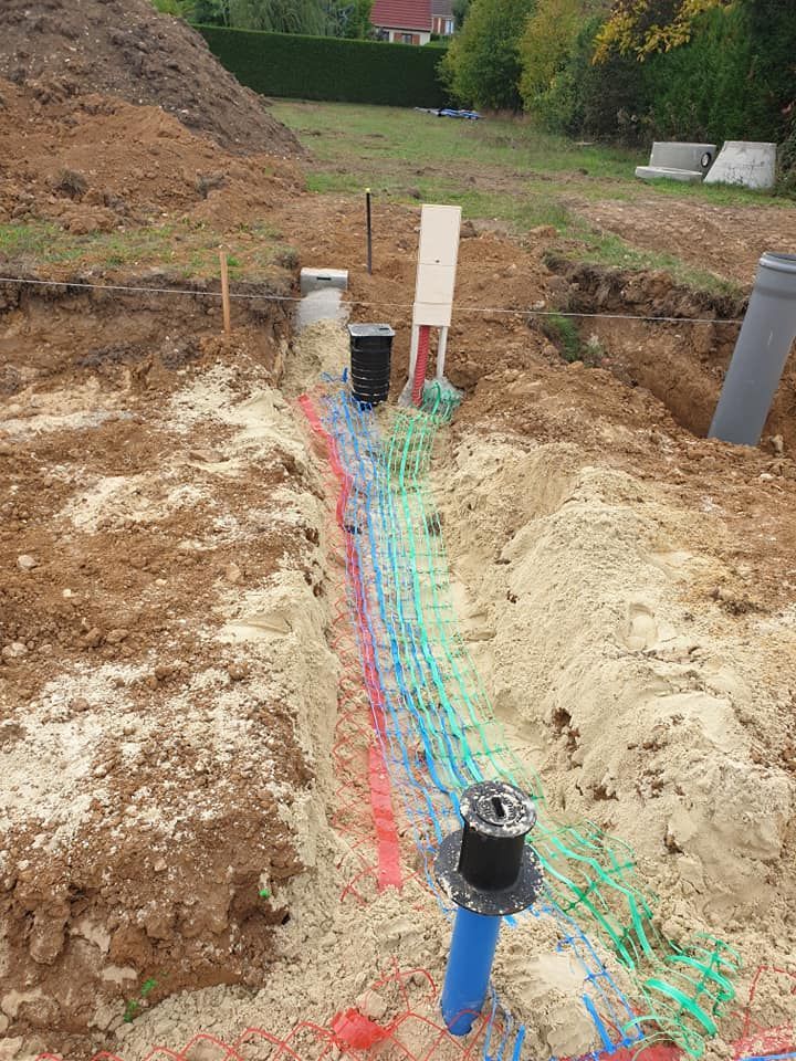 Tranchée avec conduits et tuyaux de protection colorés, avec boîtes de raccordement visibles, sur un chantier de construction en terre.