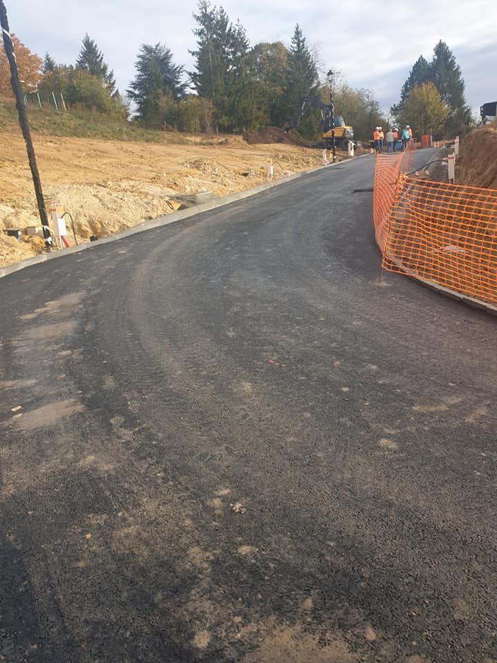 Une route asphaltée fraîchement refaite serpente vers le haut à travers un chantier de construction, bordée de clôtures de sécurité orange et de talus de terre.