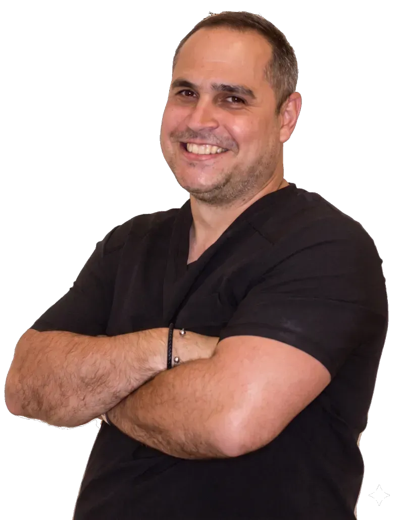 Hombre sonriente con camisa negra y brazos cruzados sobre un fondo blanco.