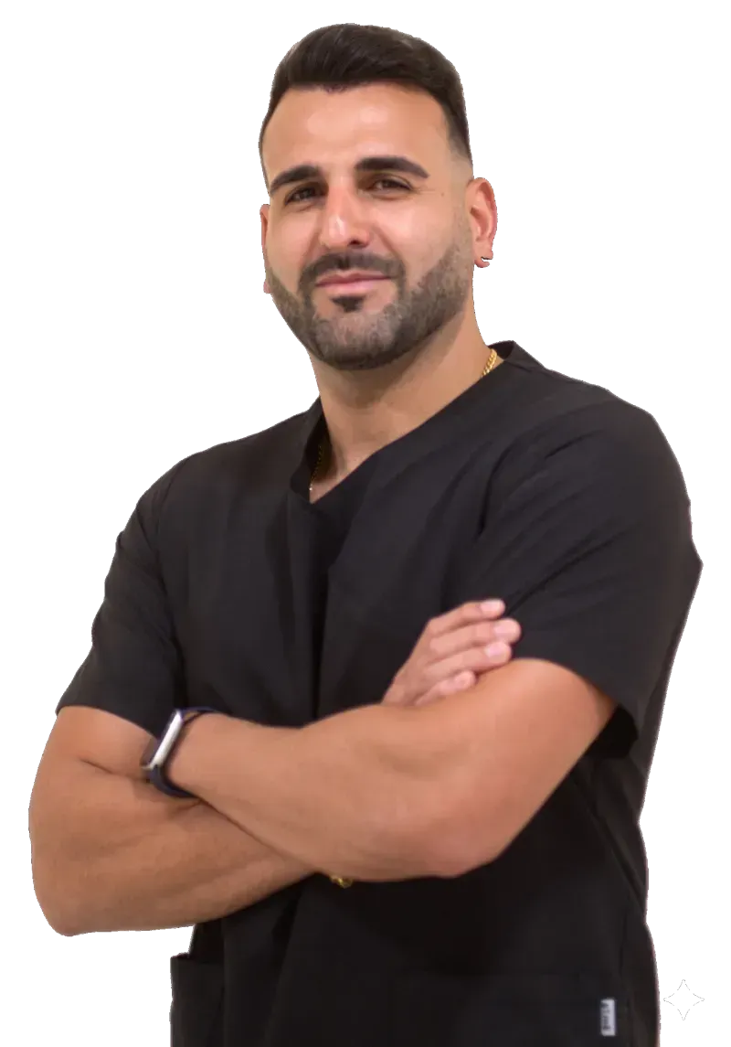 Hombre con cabello corto y oscuro y barba, vestido con una camisa negra, de pie con los brazos cruzados 