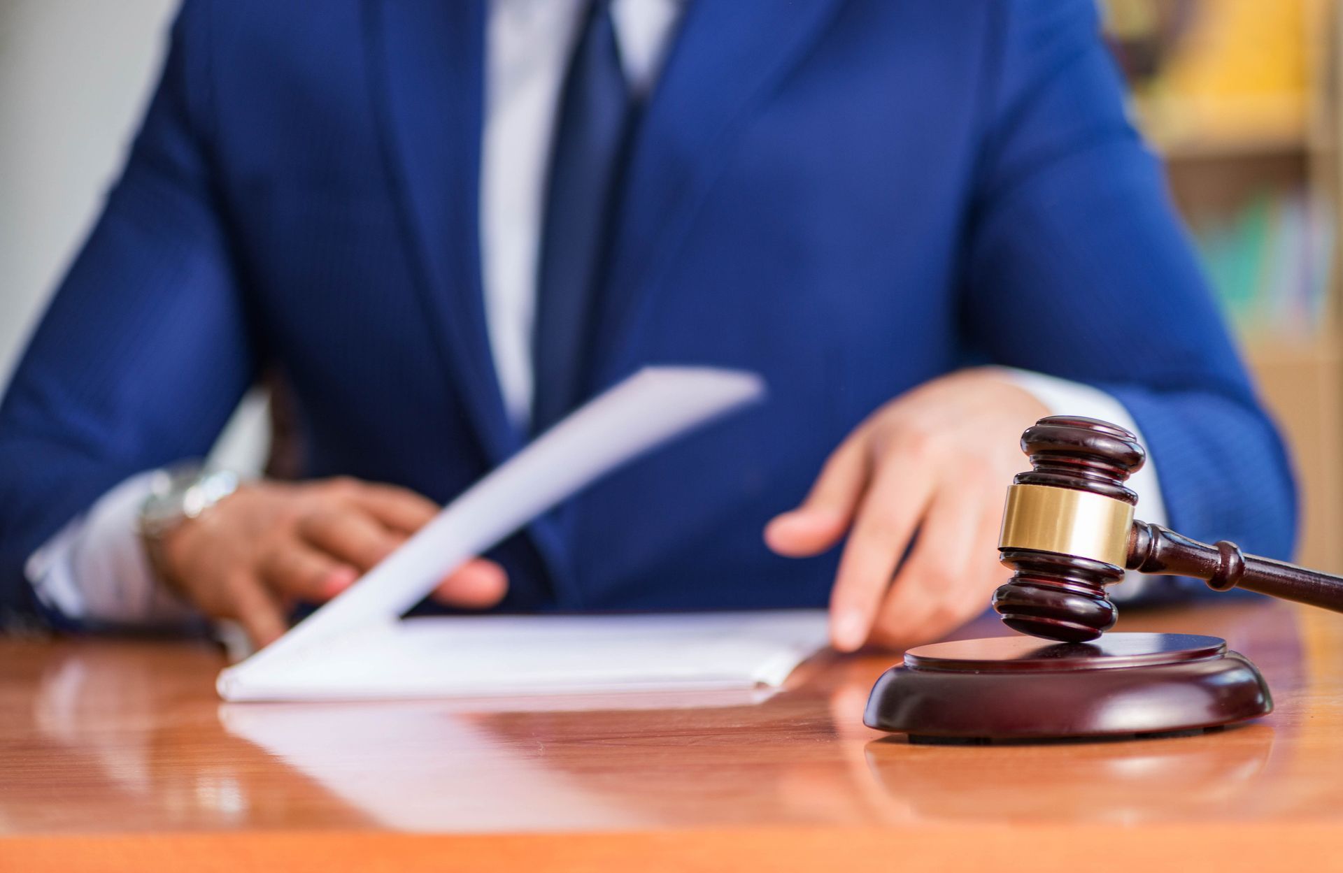 Una persona con traje azul revisa documentos en un escritorio; hay un mazo cerca.