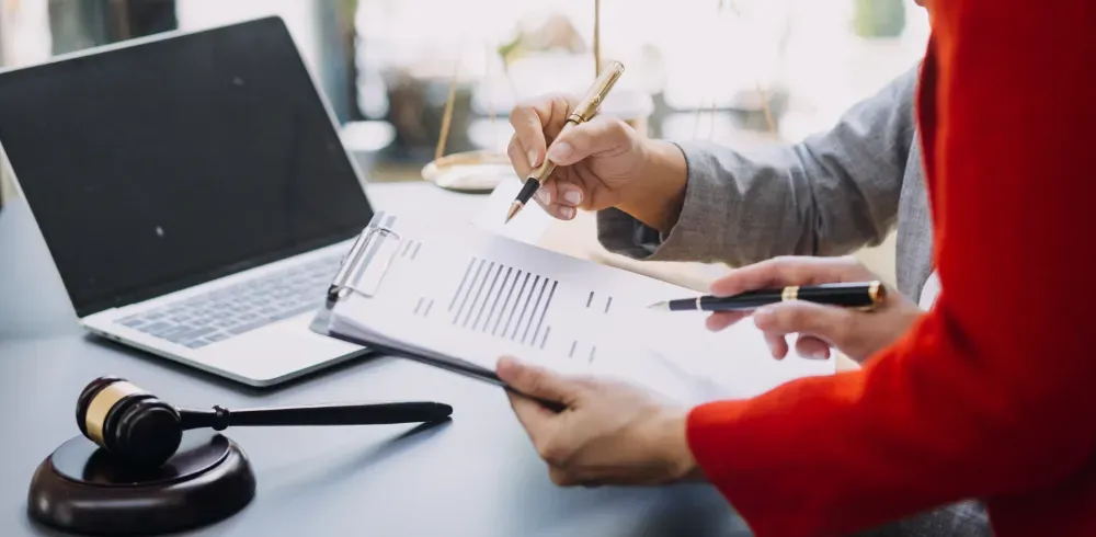 Personas revisando documentos con una laptop y un mazo sobre un escritorio. Una persona señala.