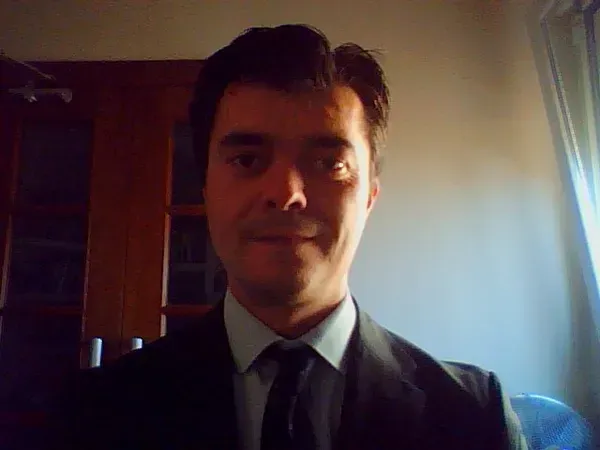 Un hombre con traje sonríe, cabello oscuro, en el interior.