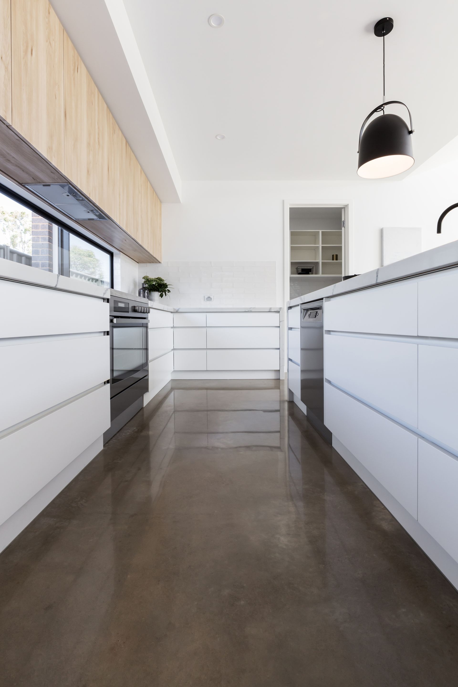 Cuisine moderne blanche avec suspension noire et sol en béton poli, vue depuis l'allée centrale.