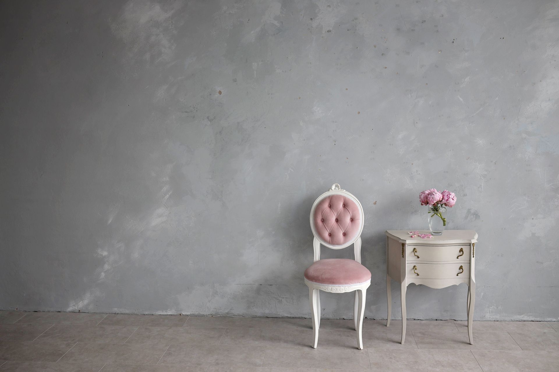 Fauteuil rose capitonné et petite table d'appoint blanche sur un mur gris.