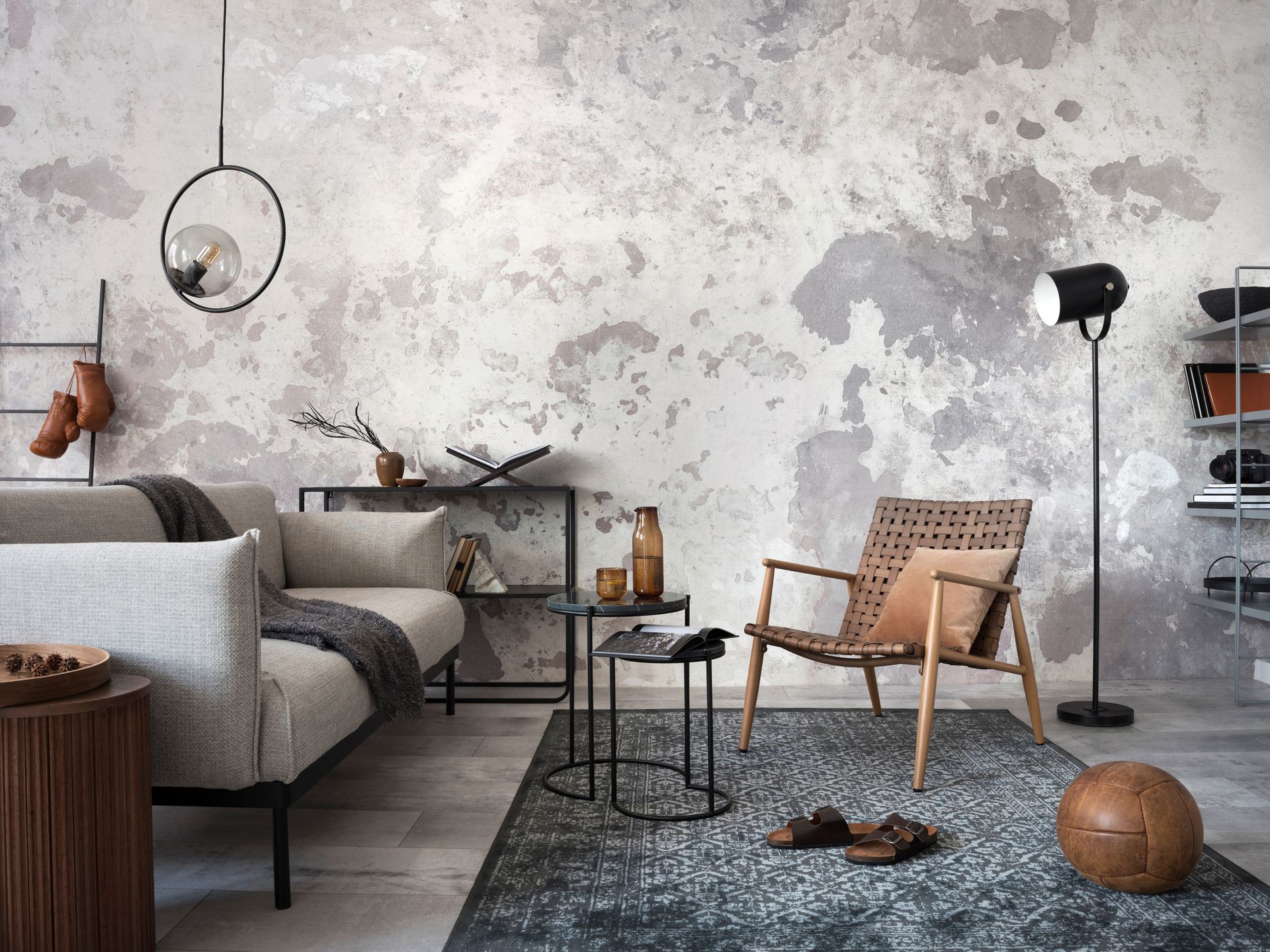 Salon avec canapé gris, fauteuil en rotin, lampadaire et tapis sur un mur texturé.