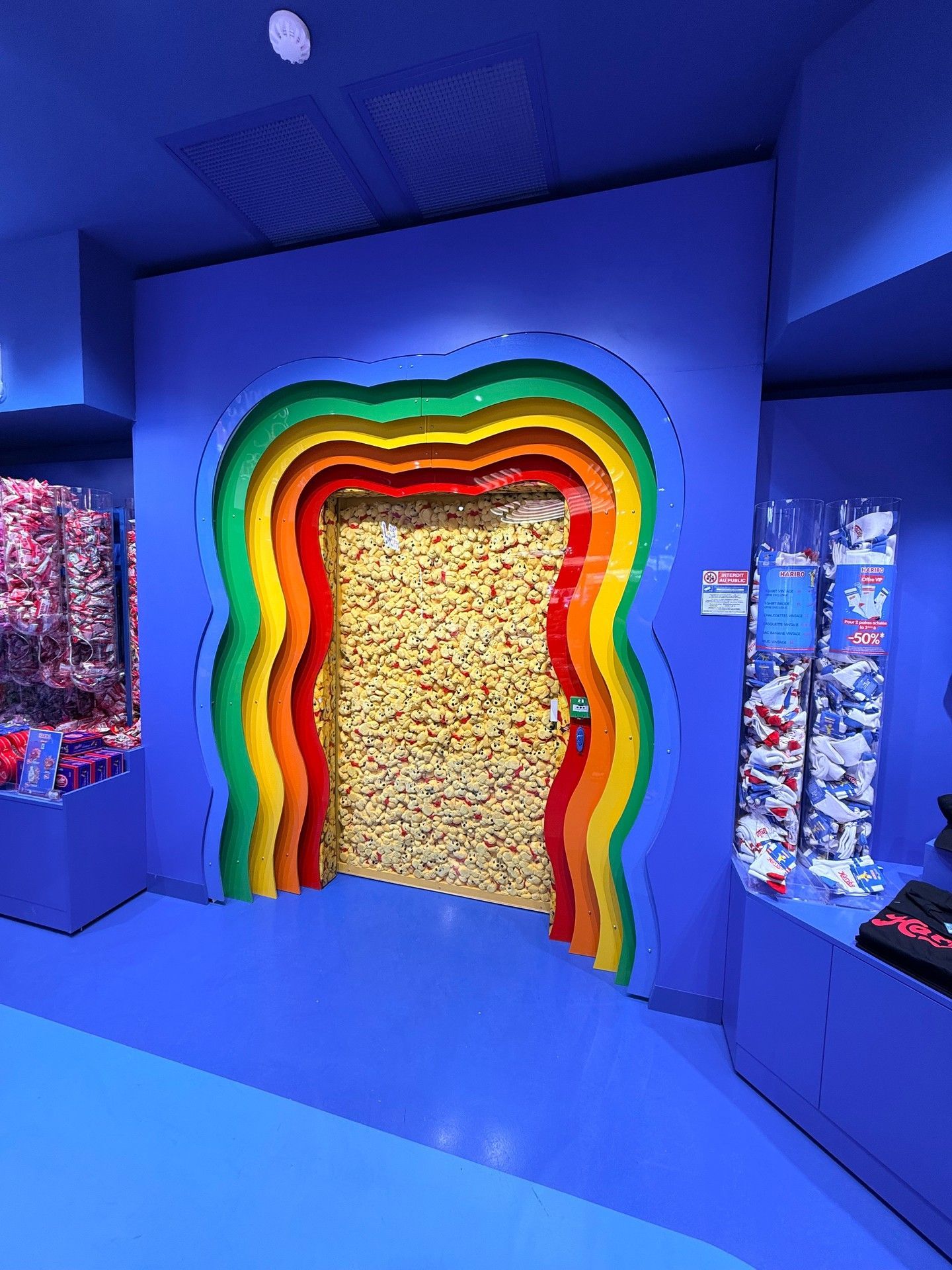 Une exposition d'un bleu éclatant avec une arche arc-en-ciel encadrant une porte texturée dans un espace évoquant un musée.