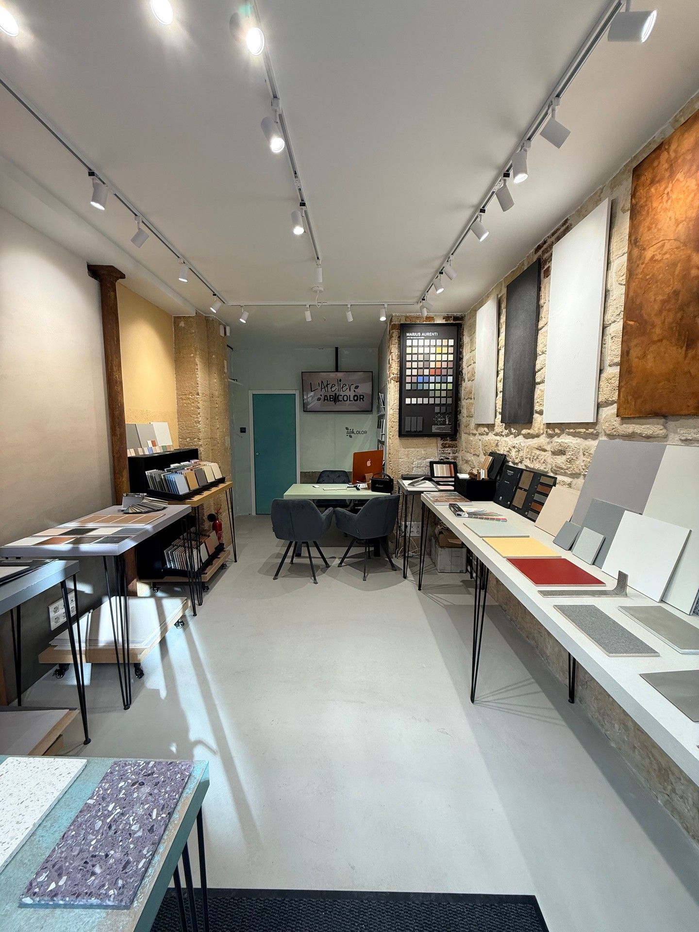 Showroom lumineux avec tables, échantillons à droite et éclairage sur rail au plafond.