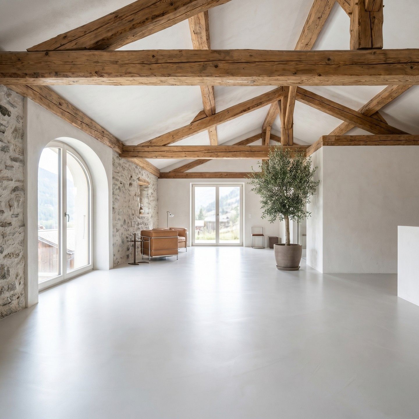 Loft moderne et lumineux avec poutres apparentes, sol blanc, fenêtre cintrée et arbuste en pot contre le mur.