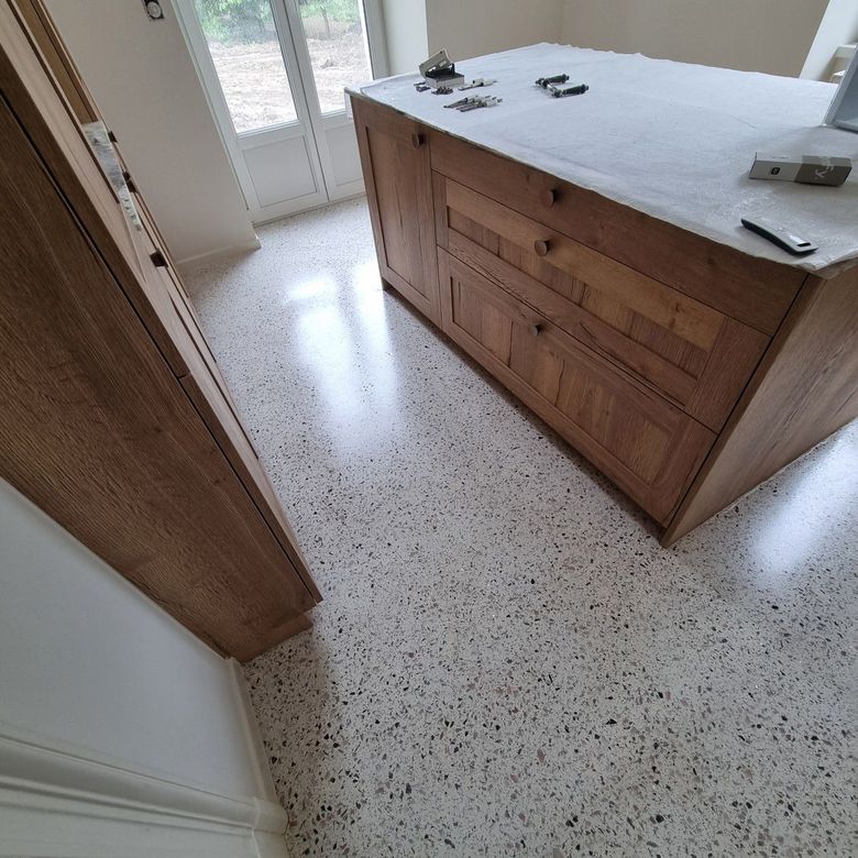 Comptoir en bois avec dessus blanc et carrelage moucheté au sol dans une pièce lumineuse.