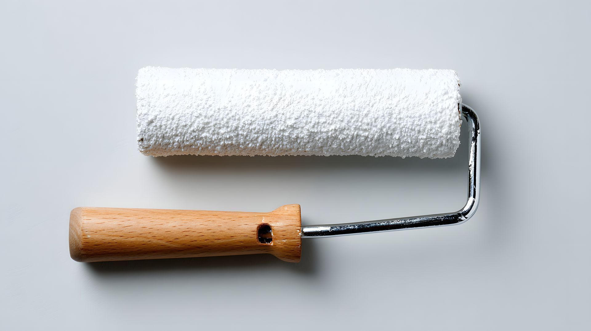 Rouleau à peinture avec de la peinture blanche et un manche en bois sur fond clair.
