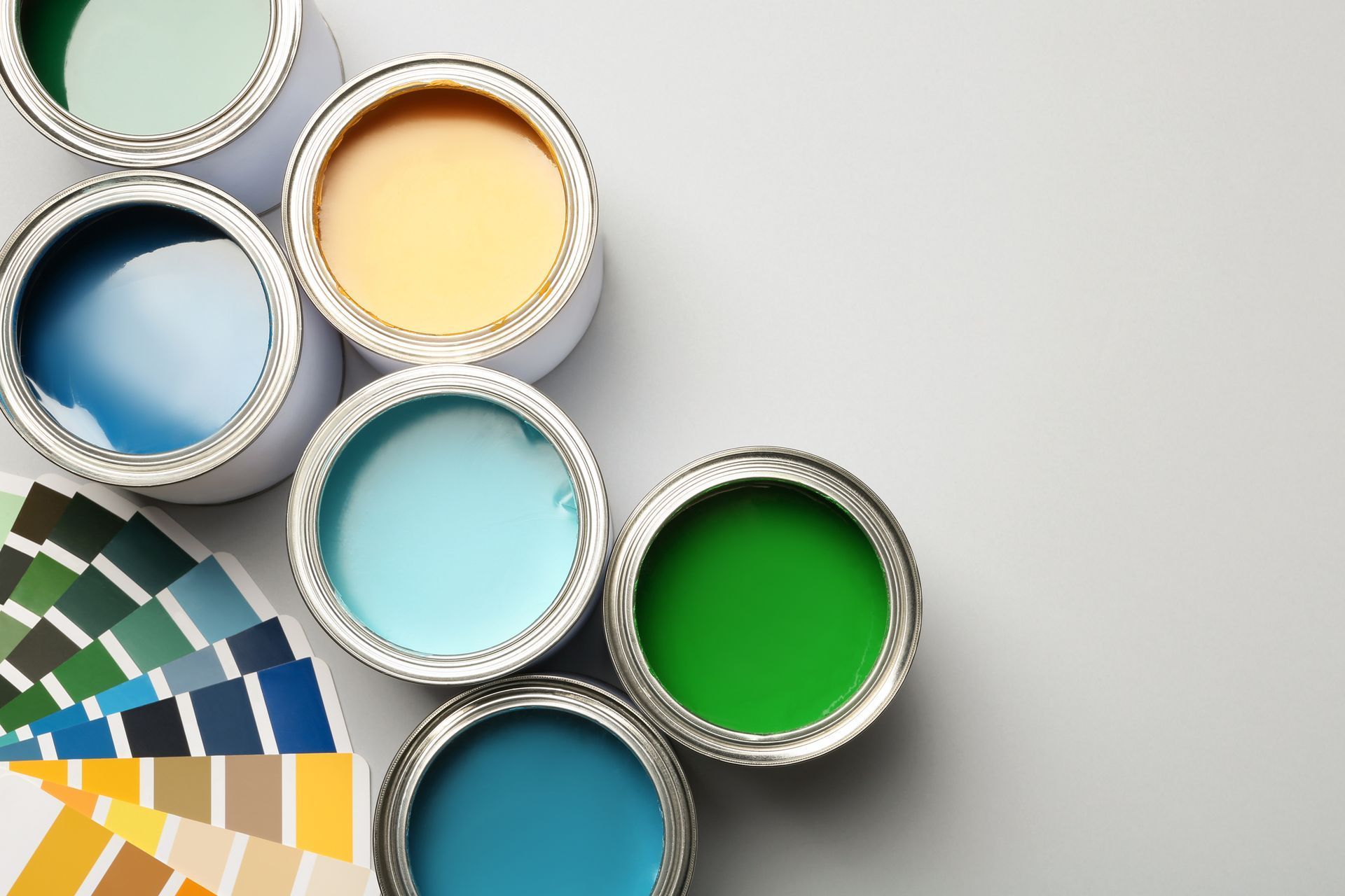 Nuancier et pots de peinture ouverts bleus, jaunes, turquoise et verts sur fond clair.