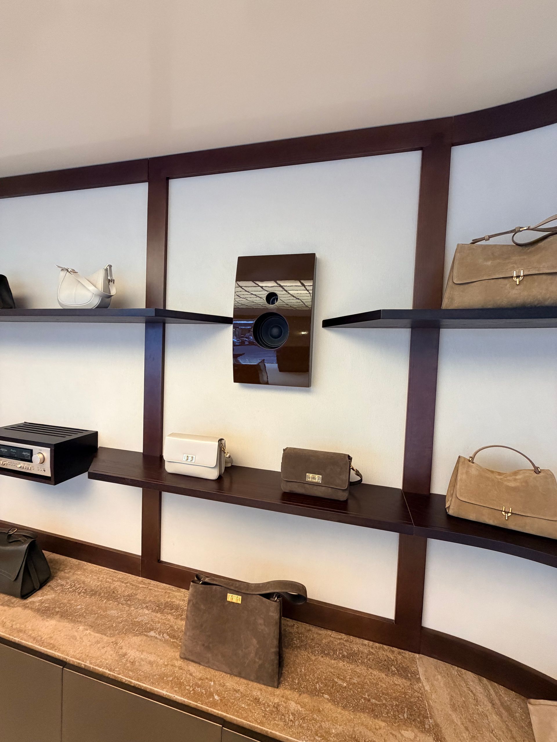 Des étagères murales aux formes arrondies mettent en valeur des sacs à main et des pochettes dans une boutique.