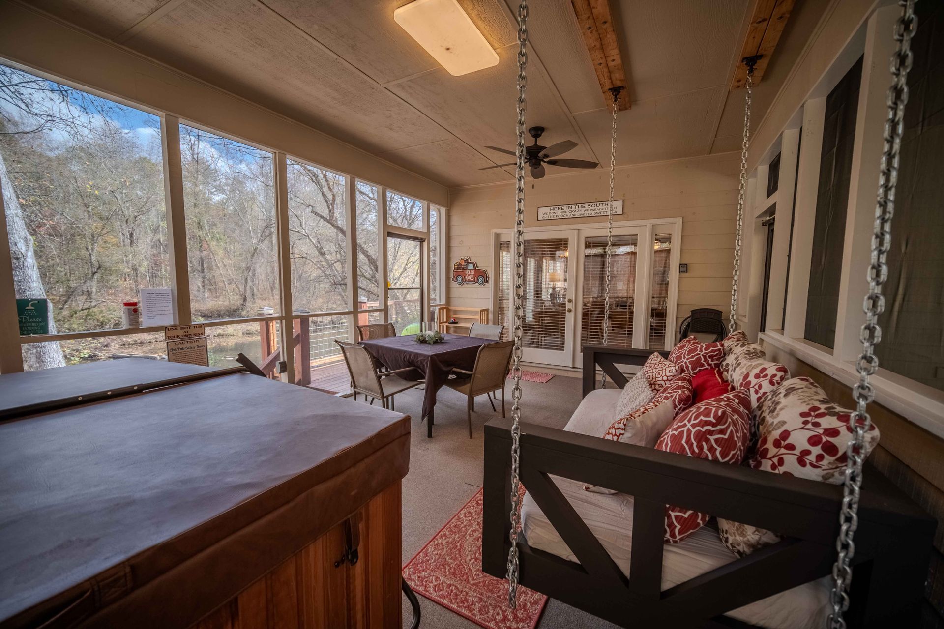 A screened in porch with a hot tub and a table. Short term rental, vacation rental, Cartecay River, fishing, Ellijay, Georgia, relax, tubing