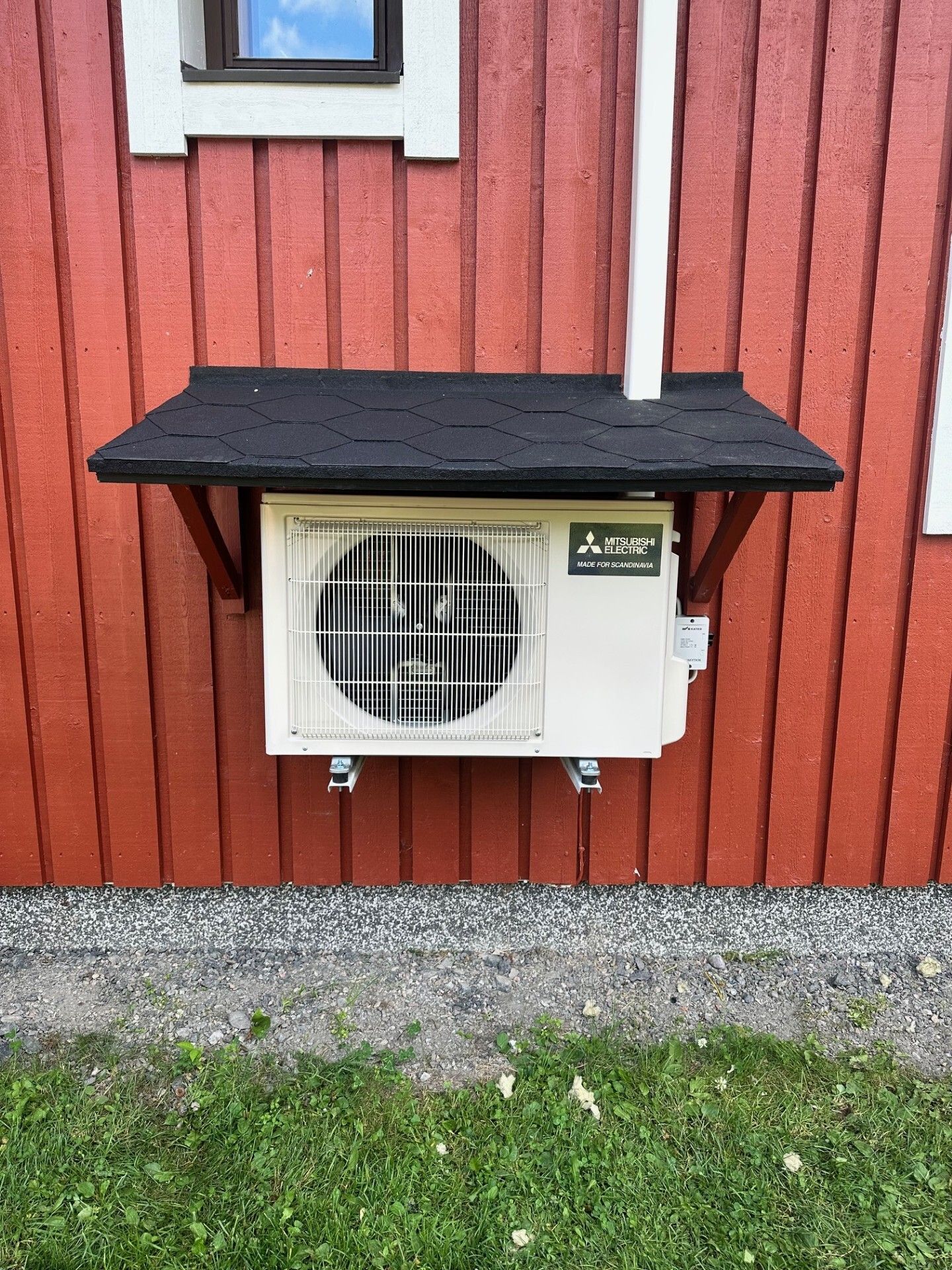 Ulkoilmastointilaite mustan markiisin alla punaisella puuseinällä