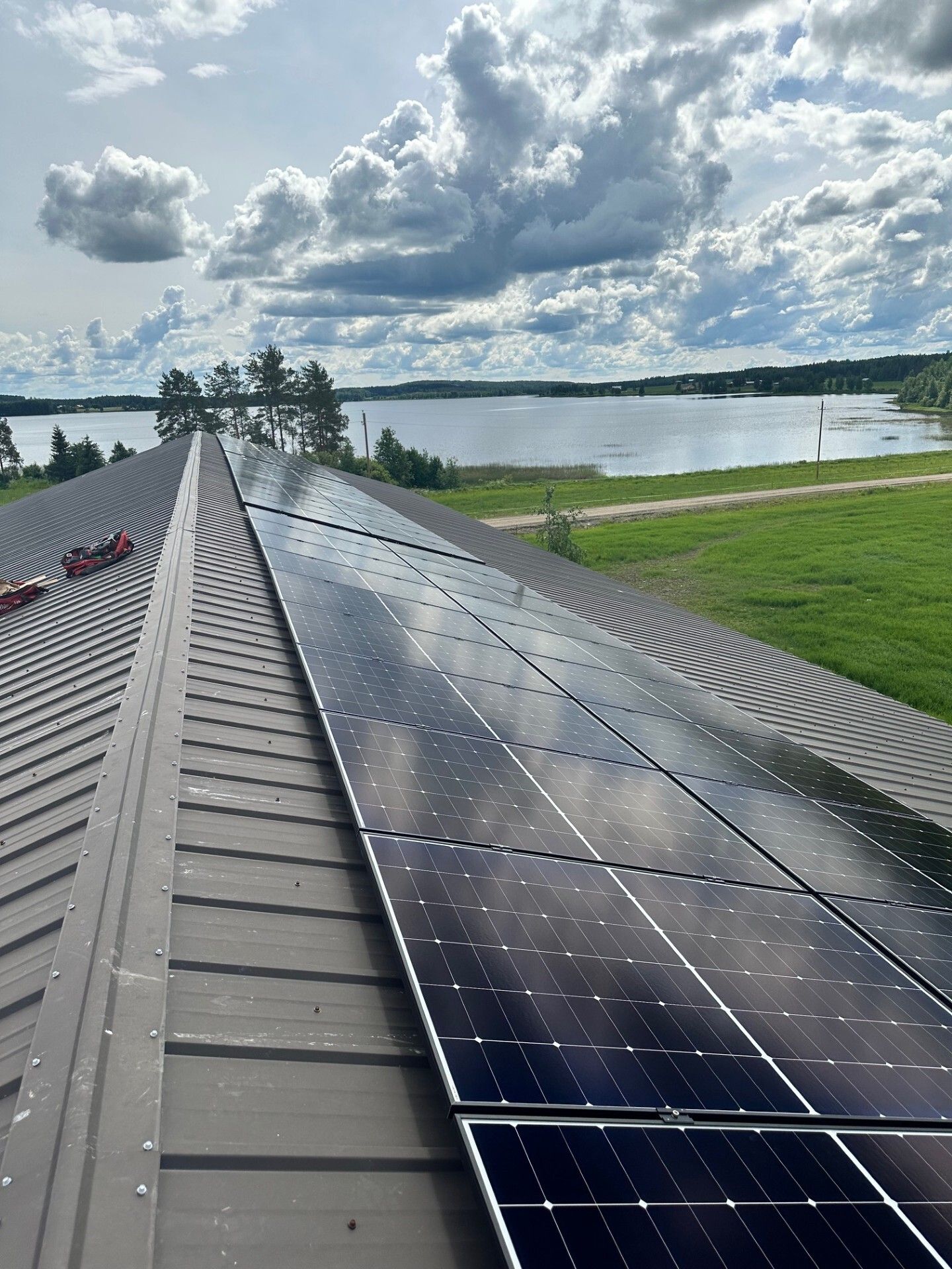Aurinkopaneelit metallikatolla järven rannalla pilvisen taivaan alla.