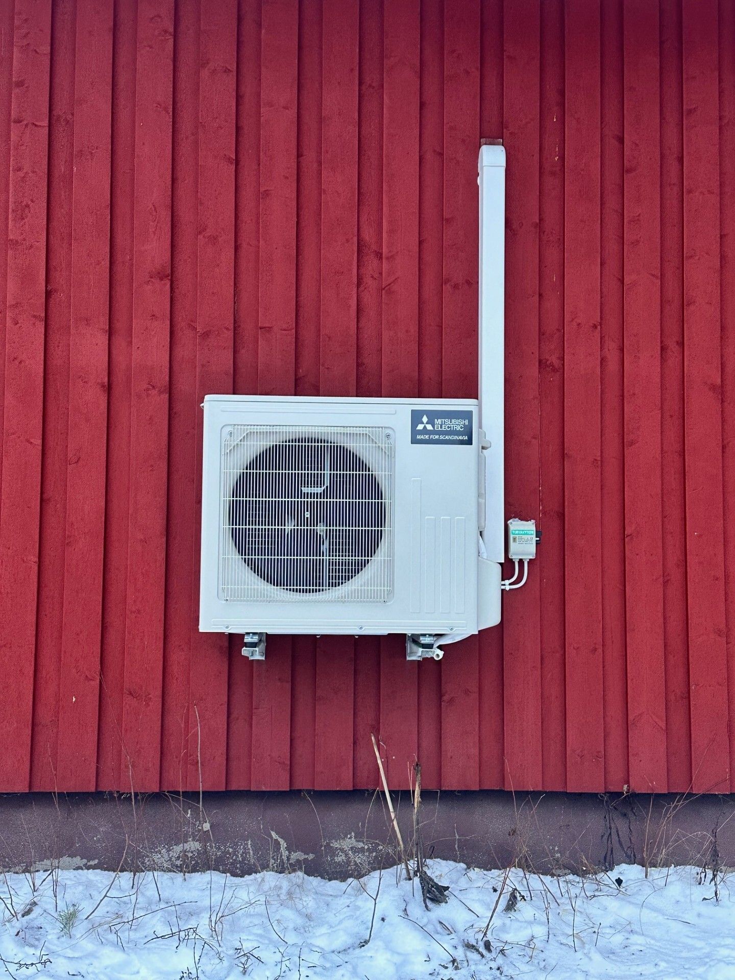 Ulkoilmastointilaite asennettuna punaiselle puuseinälle lumisen maan yläpuolelle