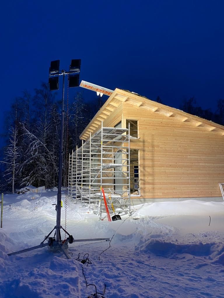 Lumen peittämä talo rakenteilla hämärässä, sen vieressä rakennustelineet ja valonheitintorni