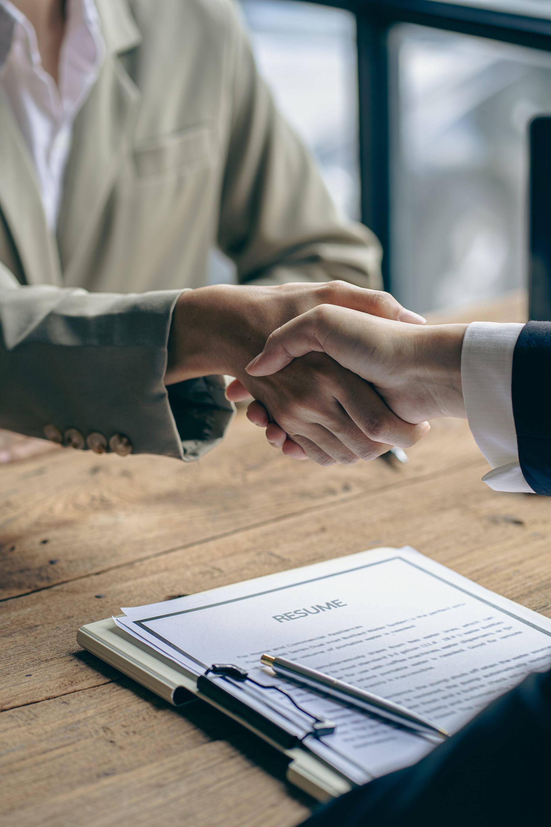 Une poignée de main au-dessus d'une table où se trouvent des documents signés, suggérant un accord commercial.