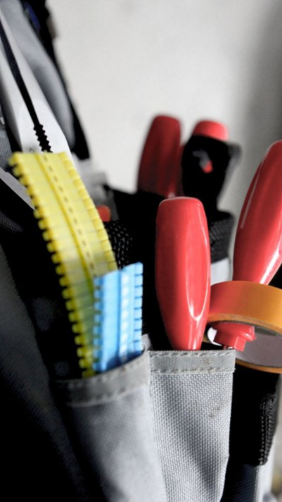 Gros plan sur des outils de bricolage avec manches rouges et jaunes rangés dans une poche de ceinture.
