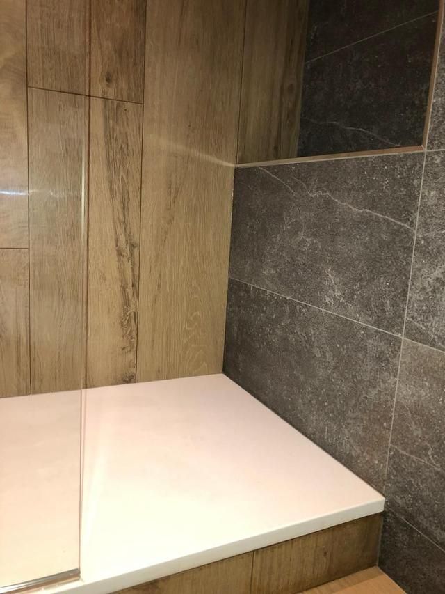 Coin douche avec siège blanc, carrelage imitation bois et carrelage en pierre gris foncé.