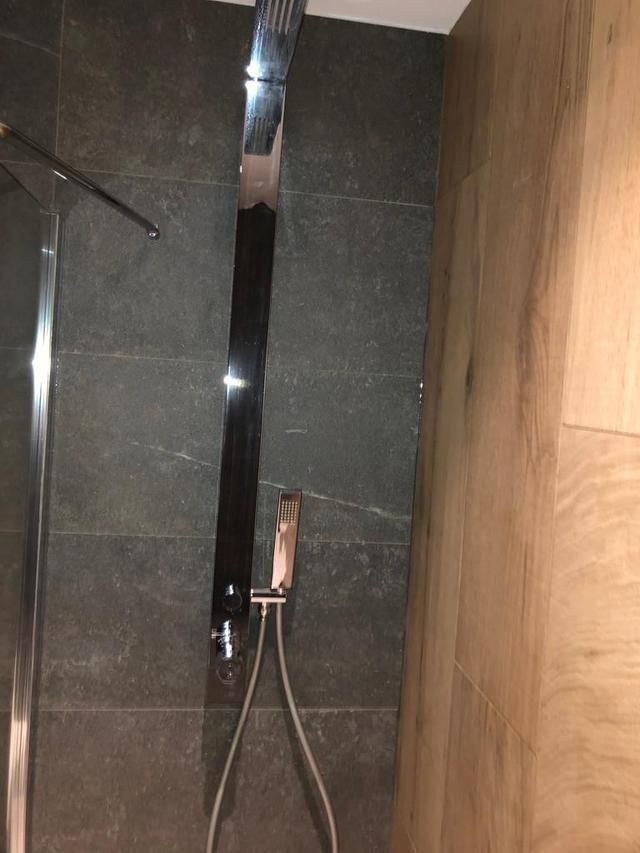 Douche avec une haute pomme de douche chromée, une douchette et un mur carrelé gris foncé.