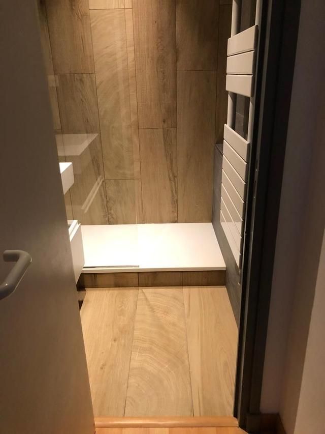 Une petite salle de bains avec une douche et un sol carrelés imitation bois. Un porte-serviettes se trouve à droite.