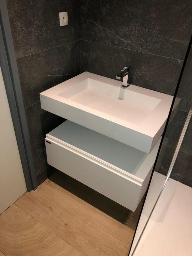 Lavabo de salle de bain moderne blanc avec meuble sous-vasque contre un mur carrelé gris foncé.