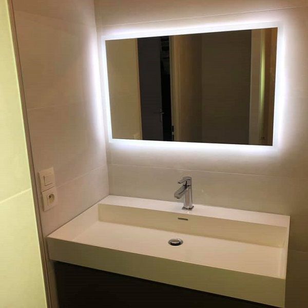 Meuble-lavabo moderne avec un miroir rectangulaire éclairé au-dessus d'un lavabo rectangulaire.