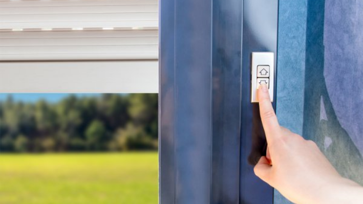 Main appuyant sur un interrupteur mural pour contrôler un volet roulant électrique.