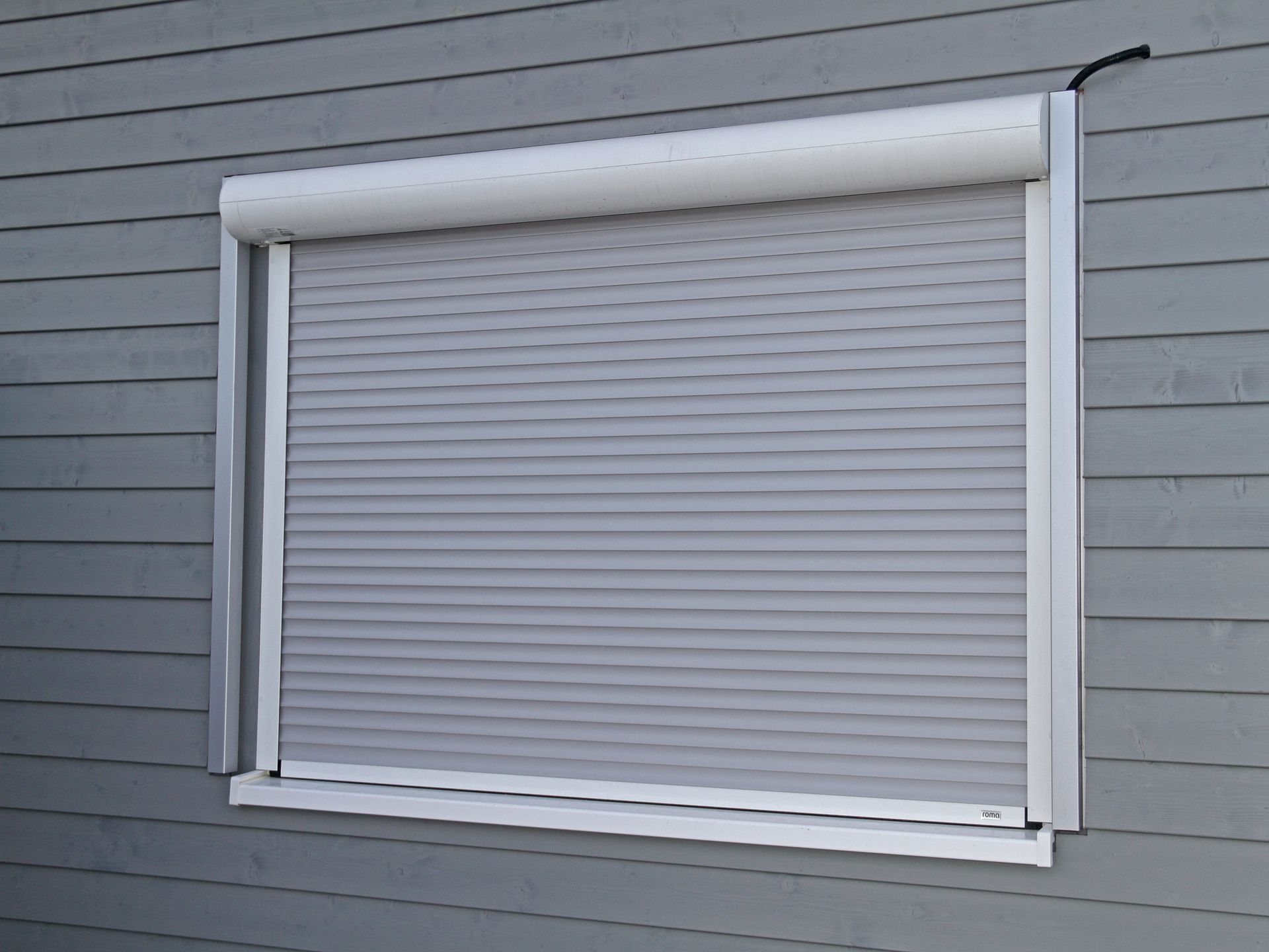 Volet roulant gris sur une fenêtre, installé sur un bâtiment en bois gris.