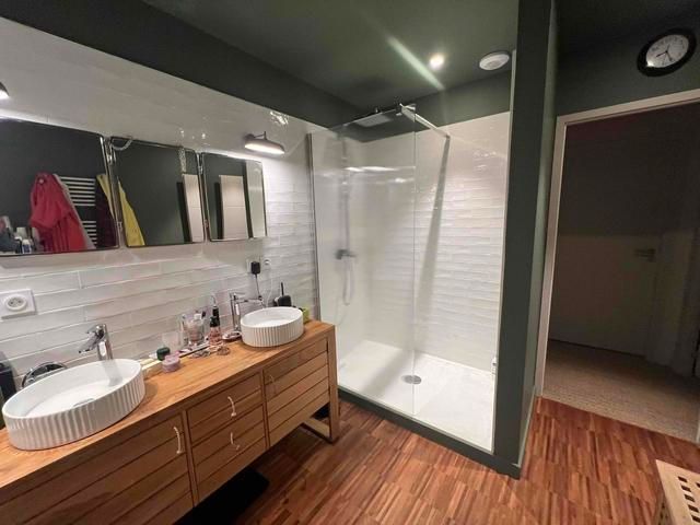 Salle de bains moderne avec meuble-lavabo en bois, lavabos blancs, carrelage métro, douche en verre et murs vert olive.