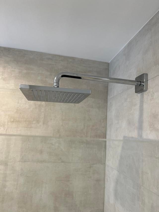 Pommeau de douche carré chromé fixé sur un mur carrelé de gris.