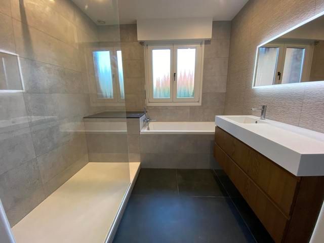 Salle de bains moderne avec carrelage gris, douche à l'italienne, meuble-lavabo en bois et fenêtre.