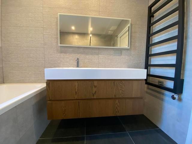 Salle de bains moderne avec meuble-lavabo suspendu en bois, lavabo blanc, miroir rectangulaire et sèche-serviettes noir.