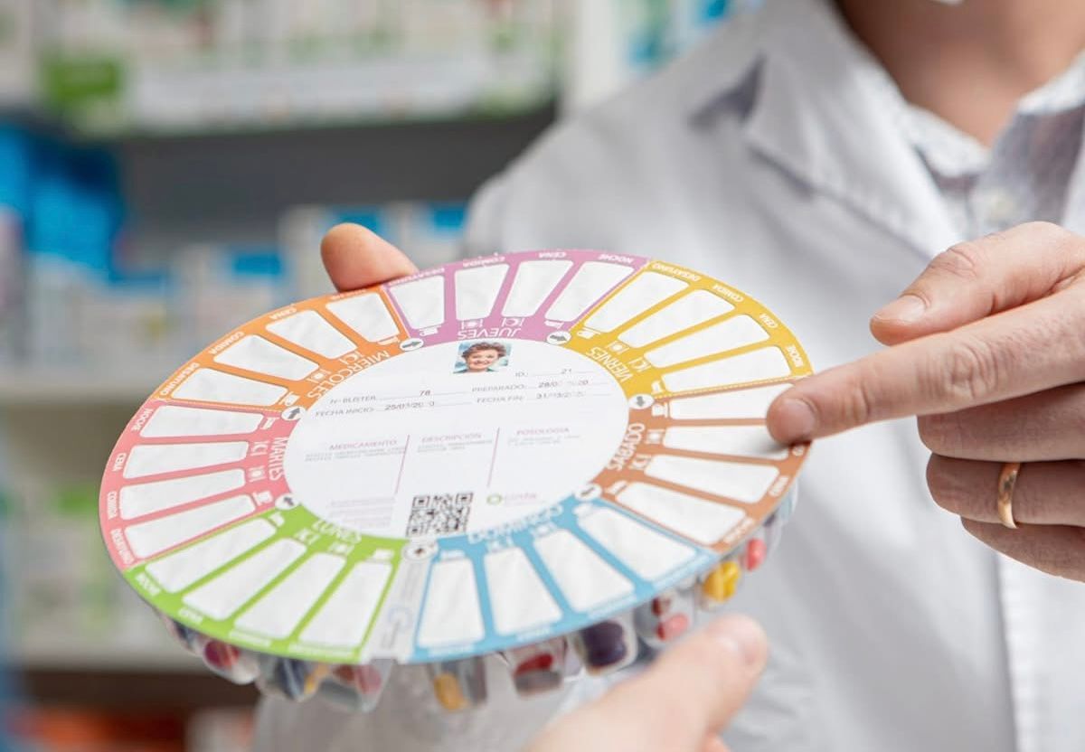 Un farmacéutico sostiene un recipiente circular colorido con pastillas.