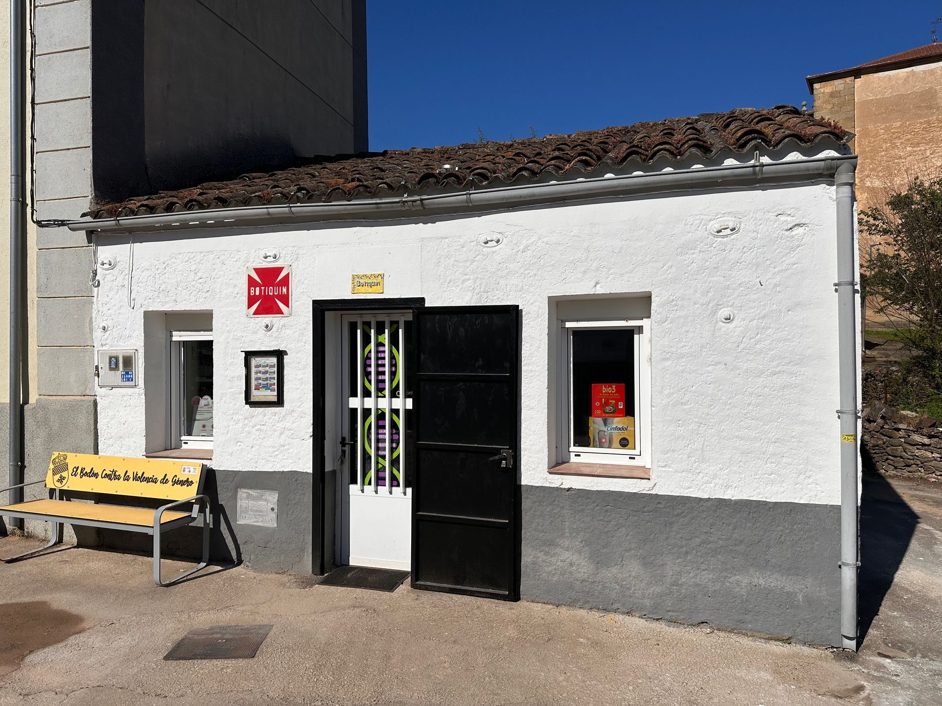 Un pequeño edificio blanco con una puerta negra y un banco amarillo delante.
