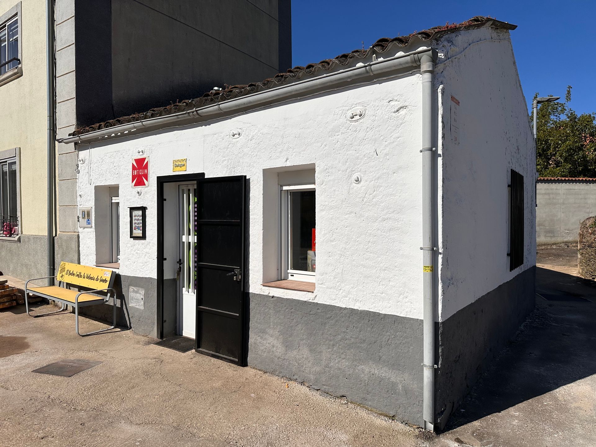 Un pequeño edificio blanco con una puerta negra y un banco amarillo delante de él.