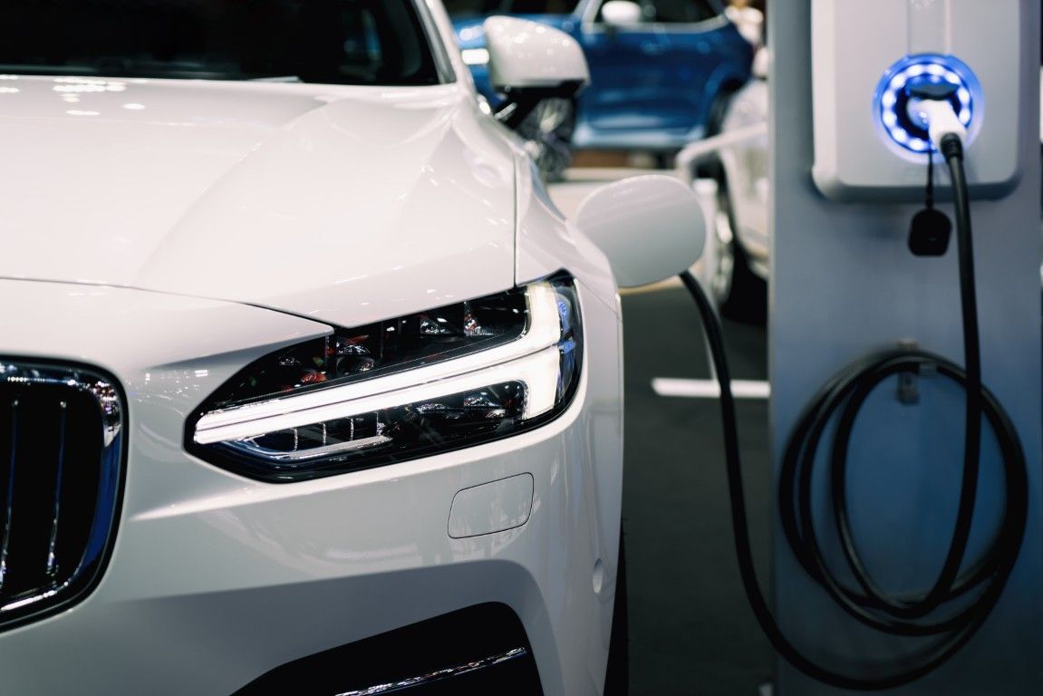 Coche eléctrico blanco cargándose en una estación cubierta.