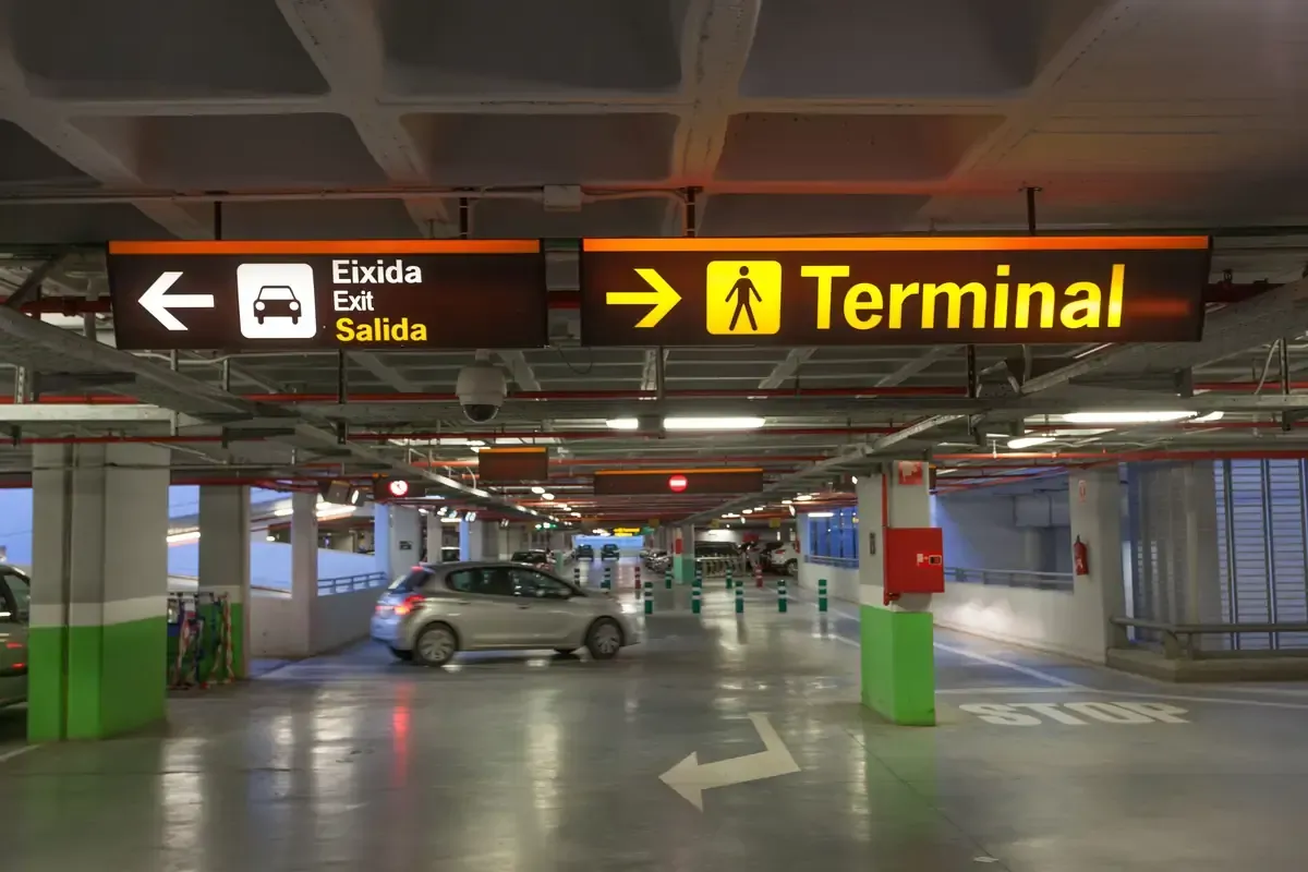 Estacionamiento cubierto con letreros que indican la salida y la terminal, y un automóvil en el carril central.