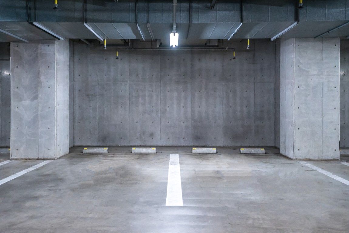 Estacionamiento cubierto con filas de autos estacionados y columnas naranjas bajo luces brillantes.