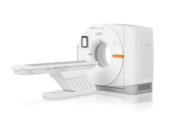Ein weißer Siemens-CT-Scanner mit orangefarbenen Akzenten, dessen Patiententisch sich vom kreisförmigen Gantry aus erstreckt.