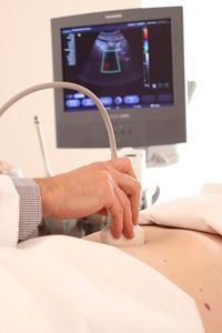 Ein Arzt führt eine Ultraschalluntersuchung des Abdomens bei einem Patienten durch, das Bild ist auf einem Monitor sichtbar.