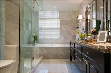 Un baño moderno con paredes de mármol, ducha con mampara de cristal, bañera integrada y lavabo doble de madera oscura.