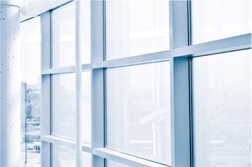 Una cuadrícula de grandes ventanales de cristal enmarcados en metal blanco, con vistas a un paisaje urbano exterior difuminado.