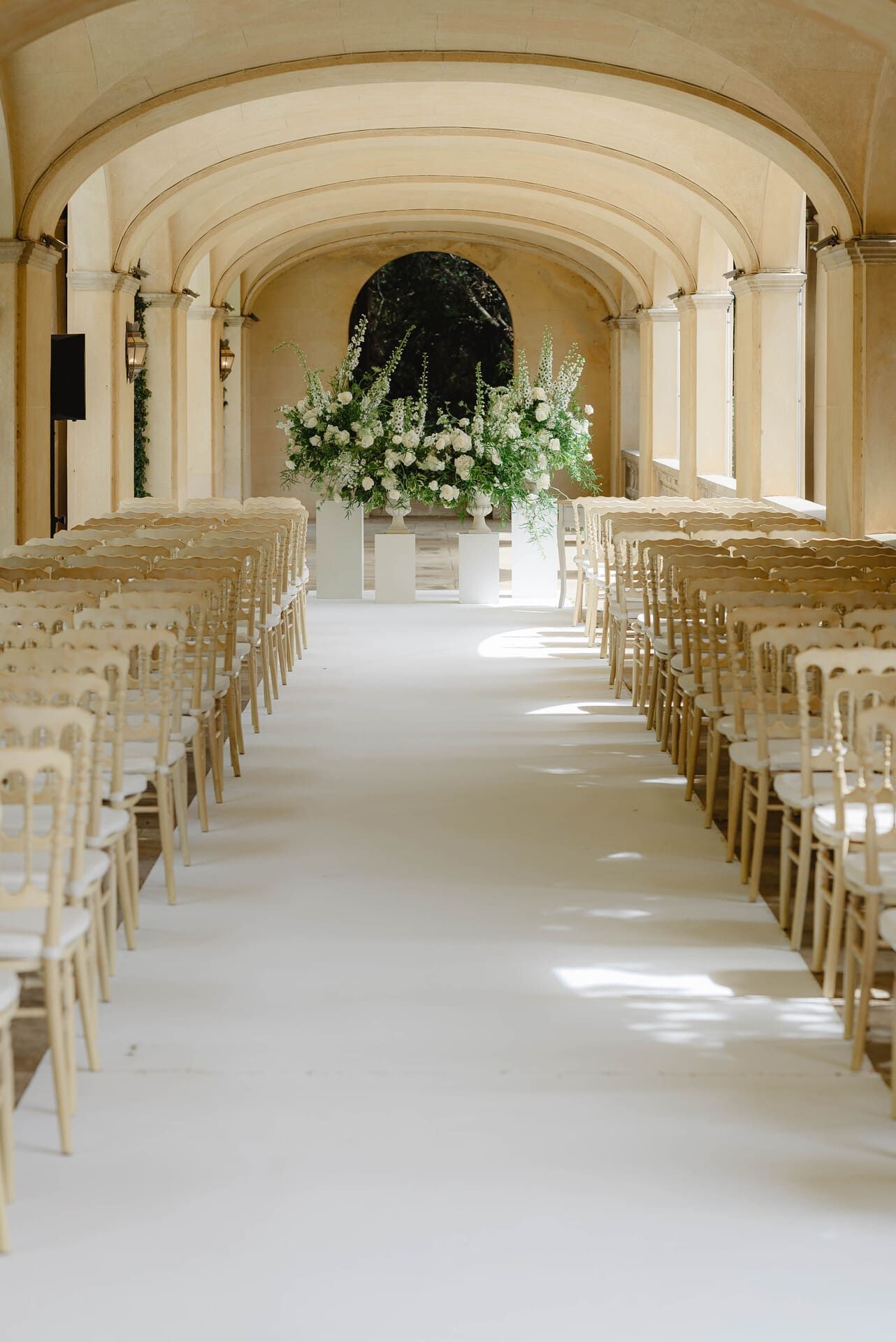 Pasillo de ceremonia con alfombra blanca, filas de sillas y arreglo floral.