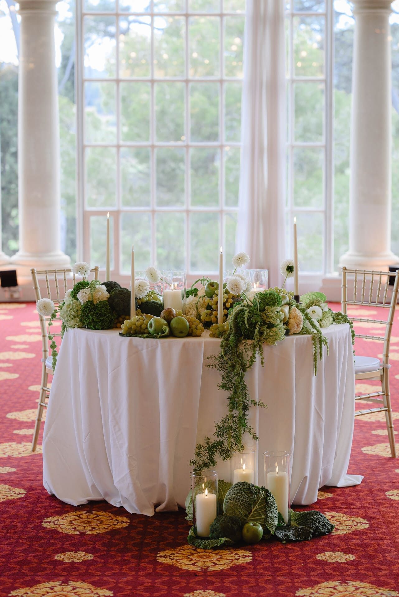 Mesa de boda con centro de flores y velas, frente a grandes ventanales.