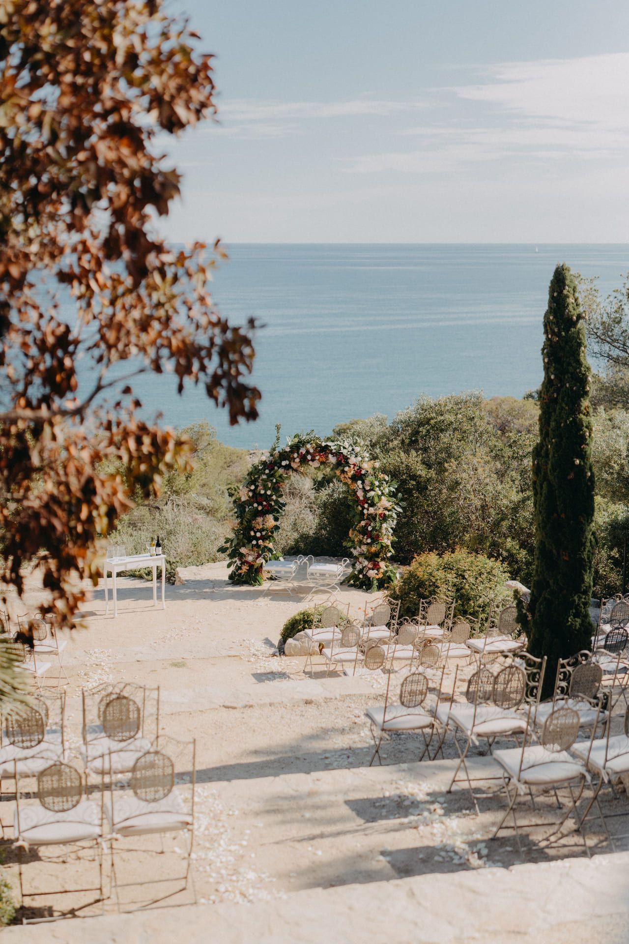 Configuración para ceremonia de boda con vista al mar: arco floral, filas de sillas, ambiente soleado al aire libre.