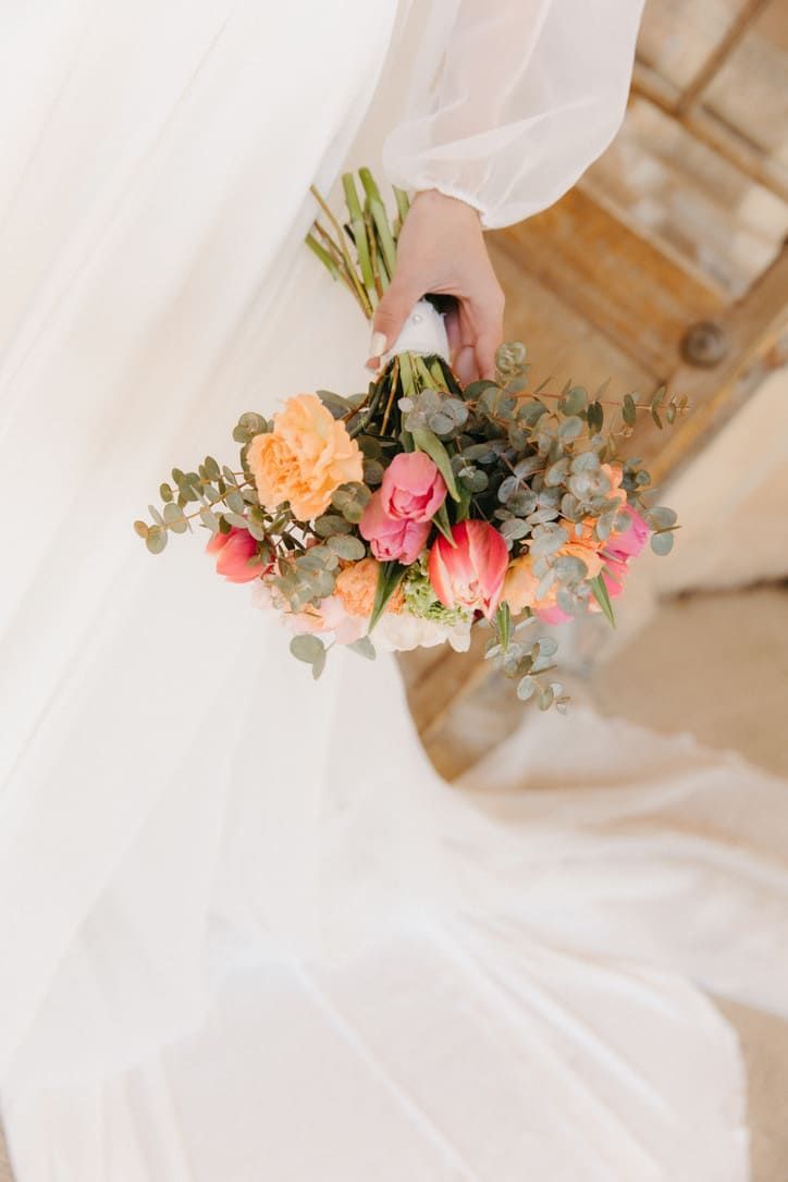 Novia sosteniendo un ramo colorido, vistiendo un vestido blanco fluido.