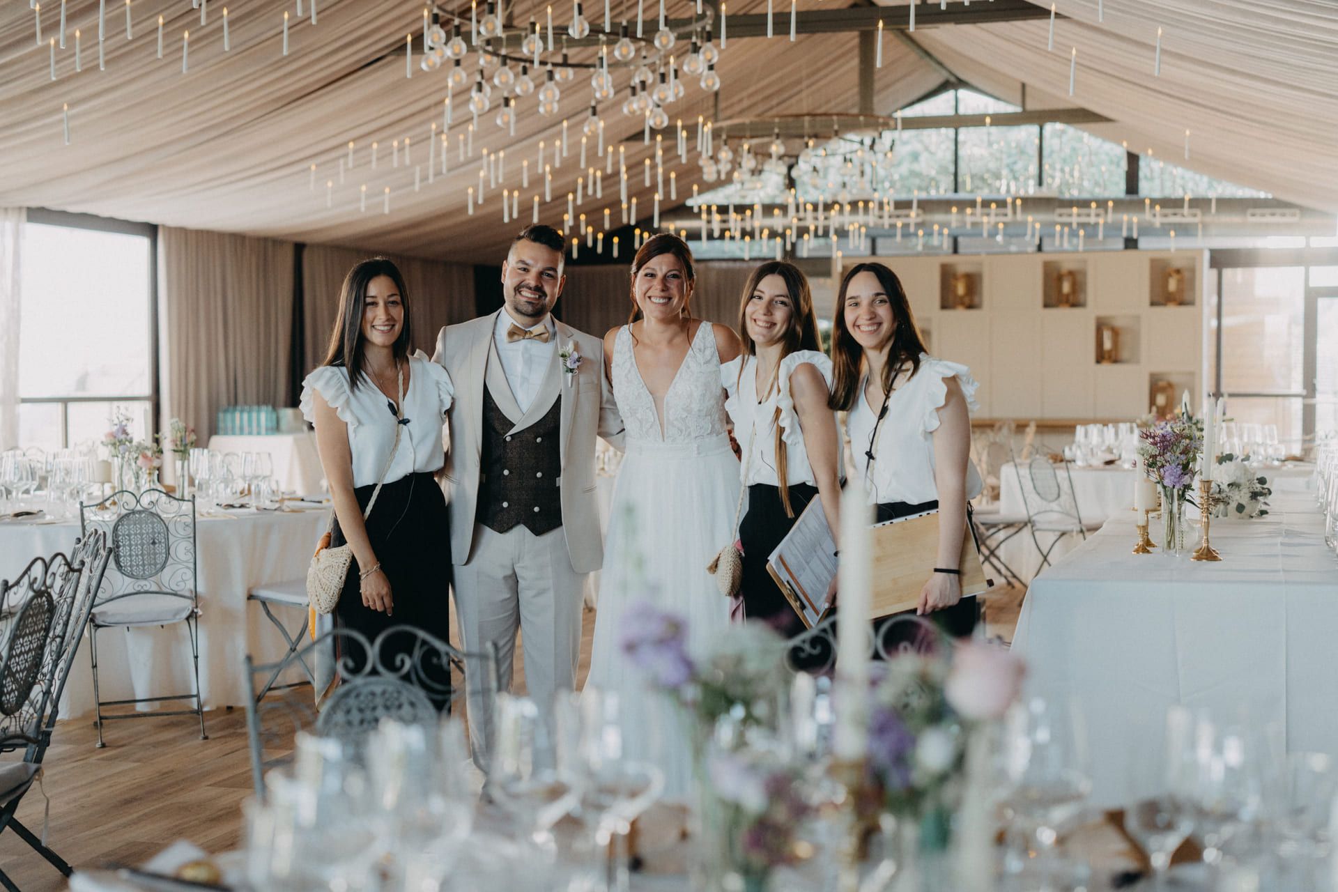 Los novios posan con los organizadores de bodas en una recepción. Sonríen. Las mesas formales están preparadas.